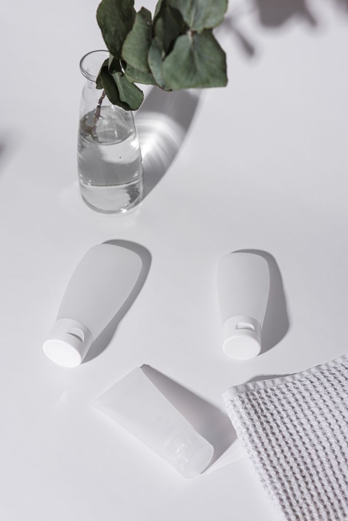 Elegant cosmetic squeeze tubes with foliage and towel on a white background.