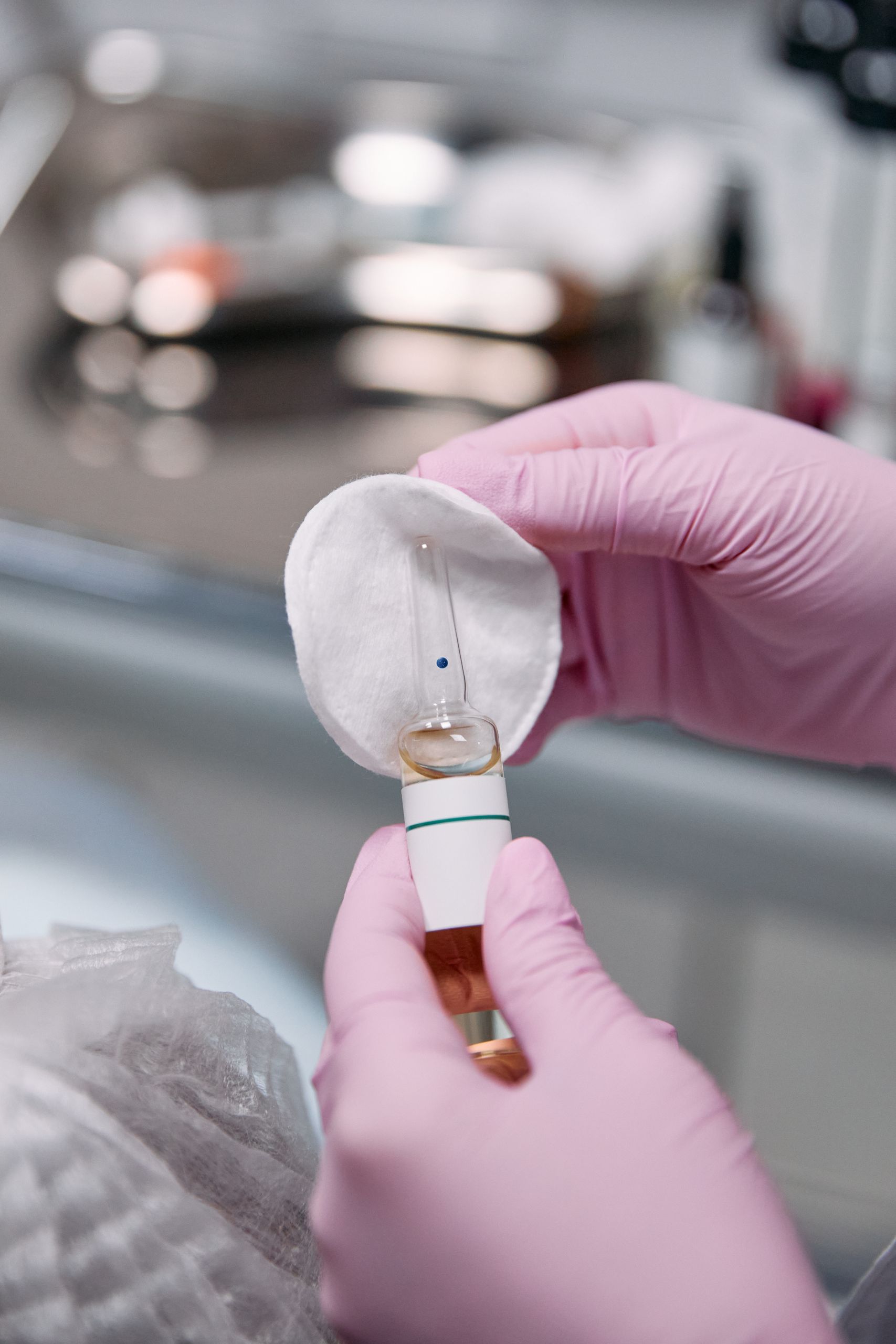 Close-up of hands in latex gloves holding a medical ampoule with cotton pad.