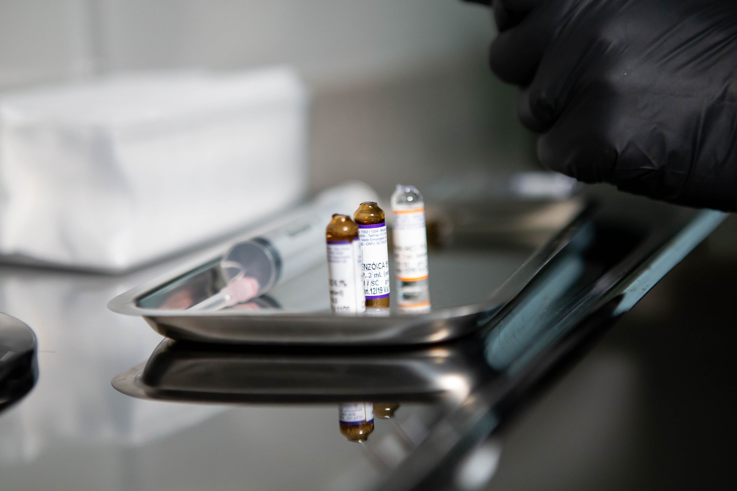 Close-up of medical vials and syringe on stainless tray in clinical setting.