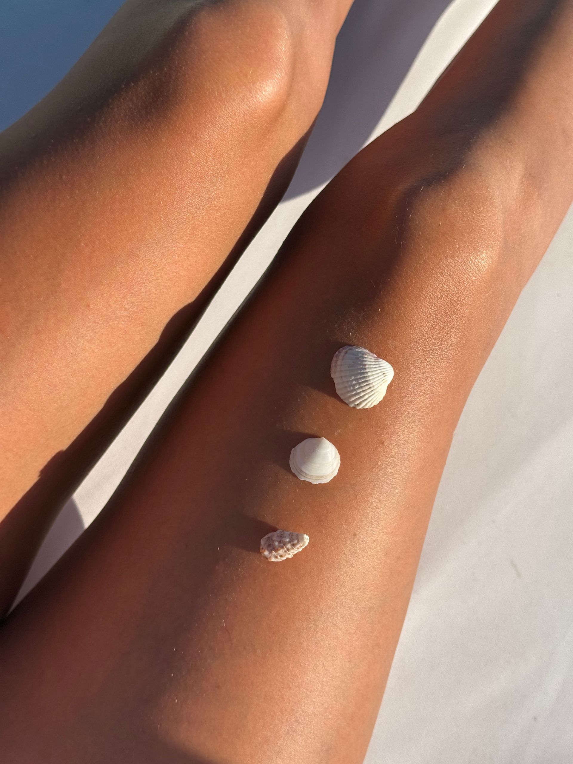 Sun-kissed legs decorated with seashells basking in the warm beach sunlight.